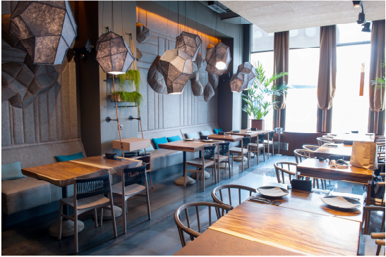Modern restaurant interior with wooden tables, chairs, and decorative hanging lights.