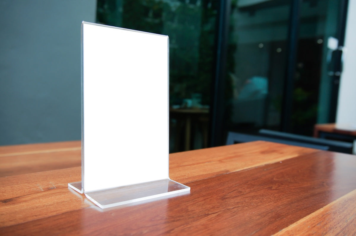 Horizontal clear acrylic menu holder with double-sided magnetic frame, displayed on a restaurant table
