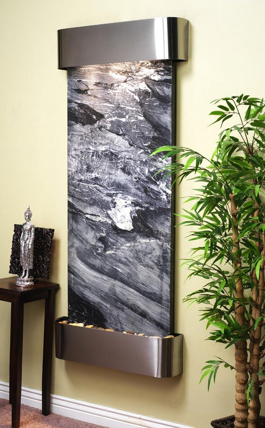 Wall-mounted water feature with marble design next to a plant and small statue on a table.